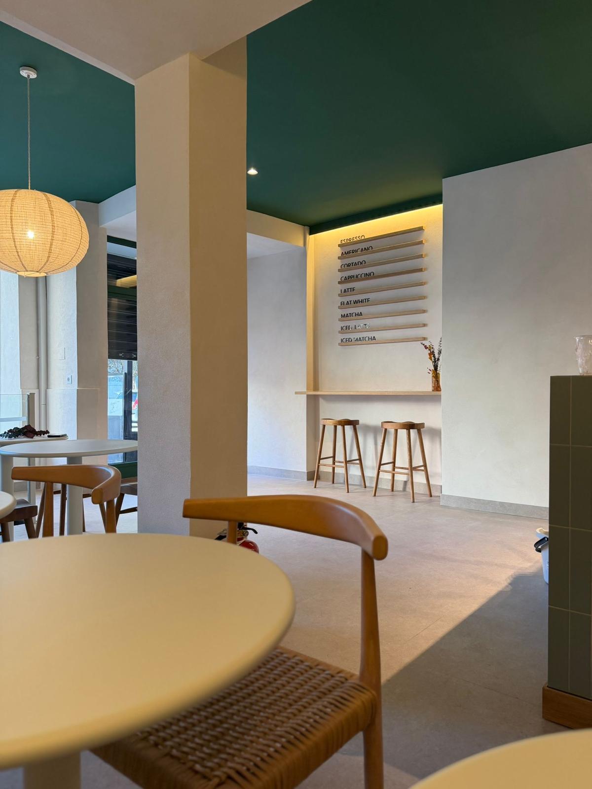 Interior de cafetería Mauna con pared verde y mesas de madera