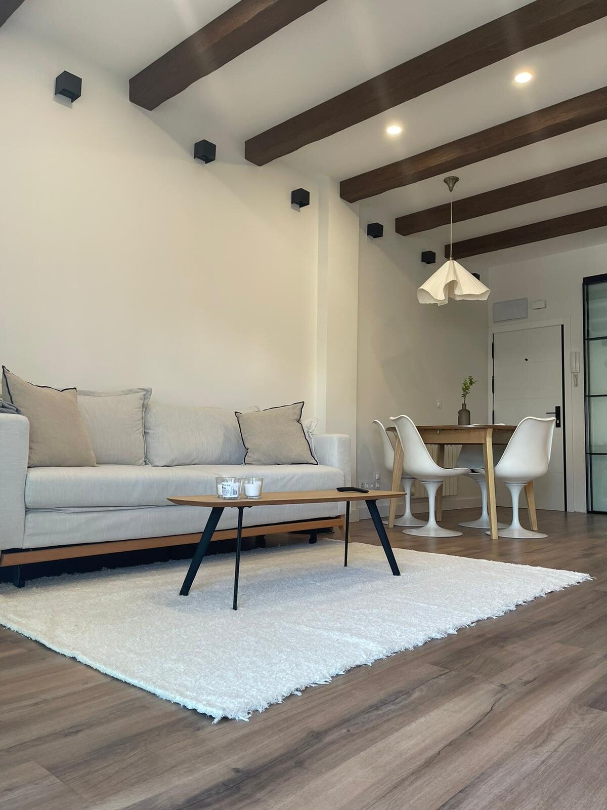Salón de vivienda en Madrid con sofá claro y vigas vistas