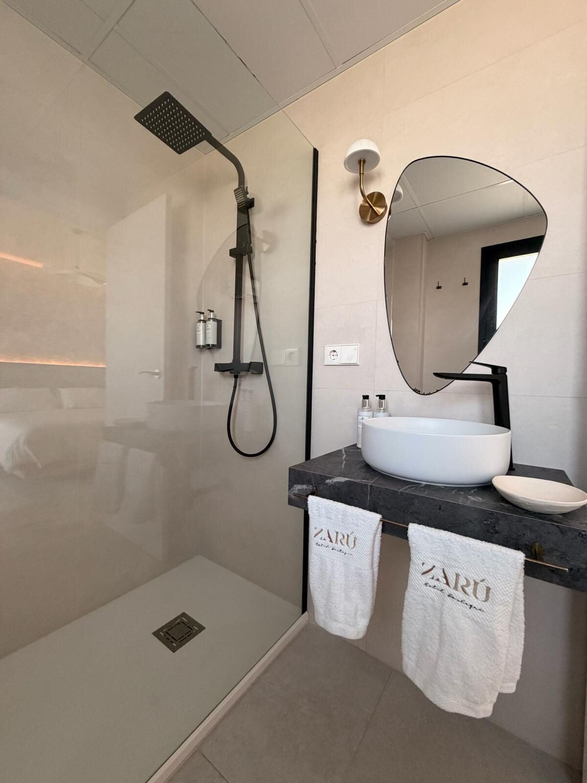 Baño del hotel Zarú con lavabo de piedra, ducha y espejo redondo